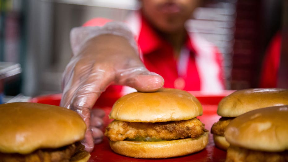 A fast food restaurant employee picks up a chicken sandwich