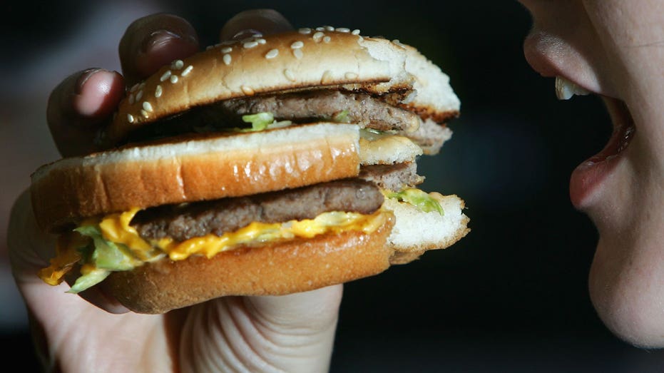 A woman eats a double cheeseburger from a accelerated nutrient chain