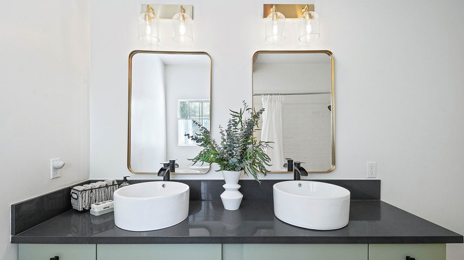 Two sinks with two mirrors and sconces and a plant in the middle on top of a black counter