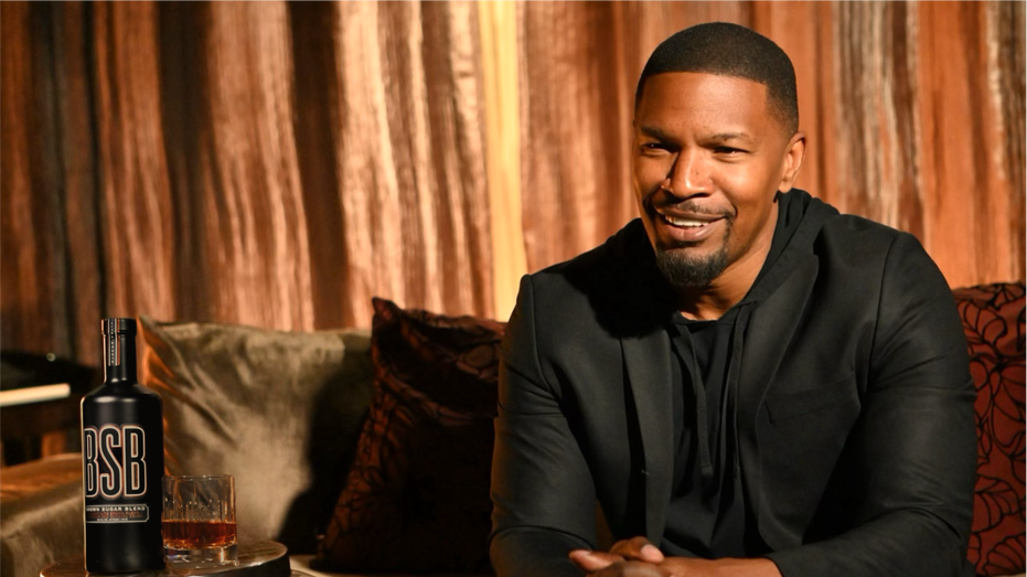 Jamie Foxx posing on a couch next to BSB Whiskey bottle