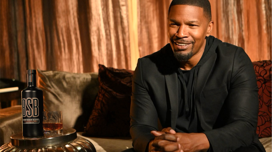 Jamie Foxx posing on a couch next to BSB Whiskey bottle