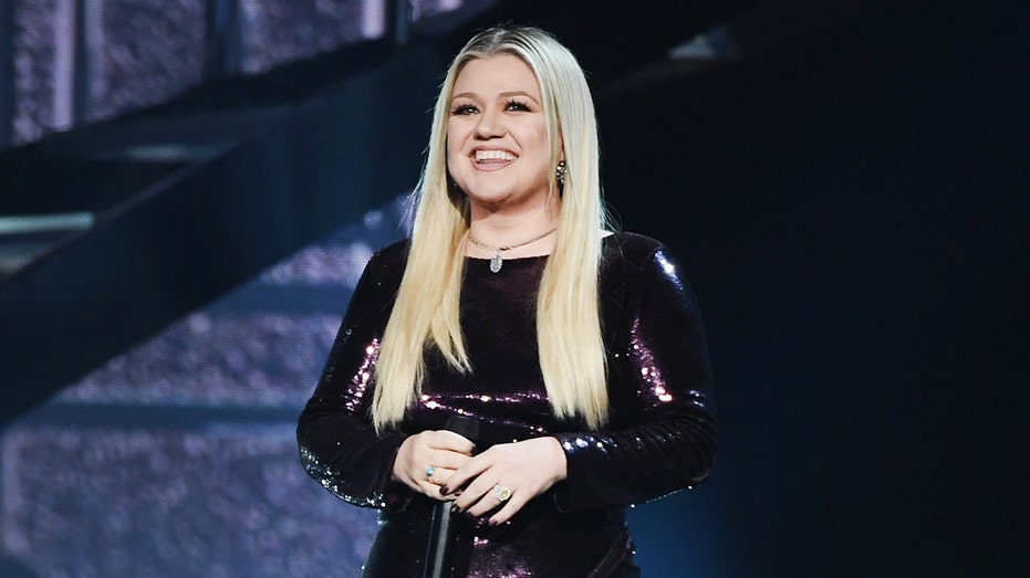 Kelly Clarkson stands on stage holding a microphone