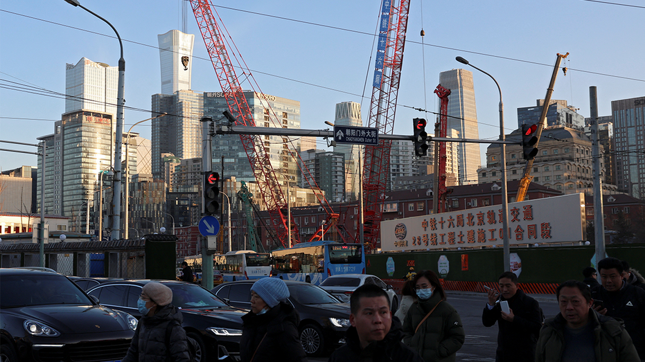 People cross an intersection near cranes standing at a construction site in Beijing.
