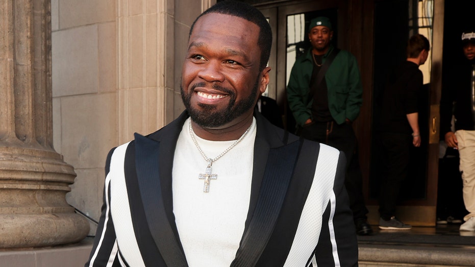 Rapper 50 Cent একটি কালো এবং সাদা ব্লেজার পরেন যার নীচে একটি সাদা শার্ট রয়েছে৷