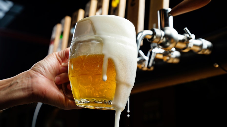 Beer is poured from a tap into a mug, which overflows with foam.