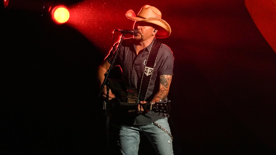 Jason Aldean holding a guitar and singing on stage