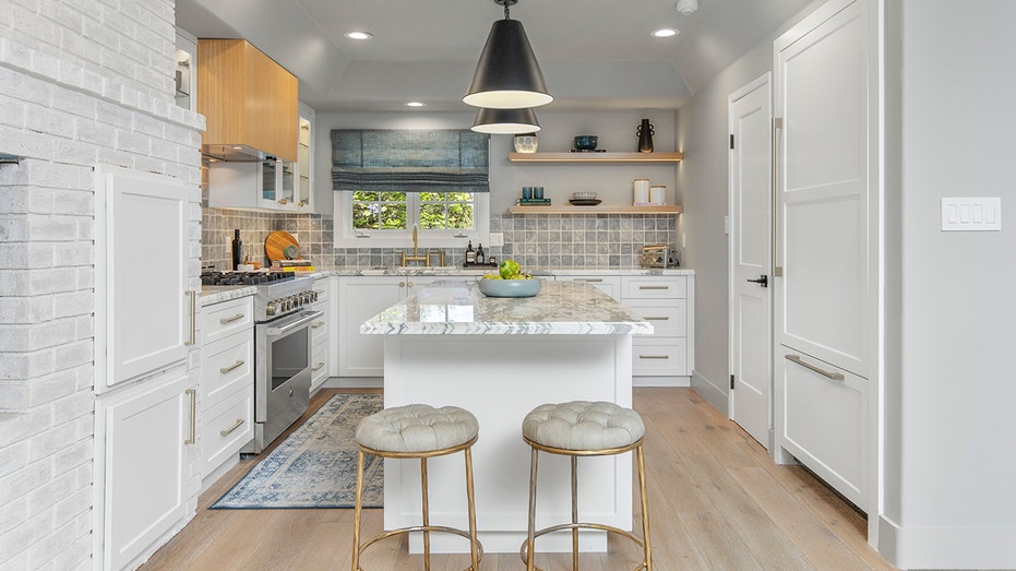 A kitchen with white cabinets, marble countertops and shelving