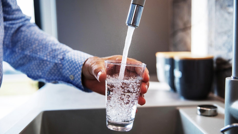 A person fills a glass with water from the sink in their home.