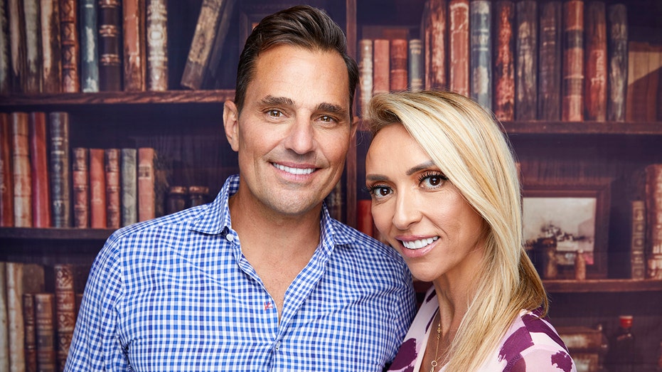 Bill Rancic in a blue checkered shirt and Giuliana Rancic smile for a photo