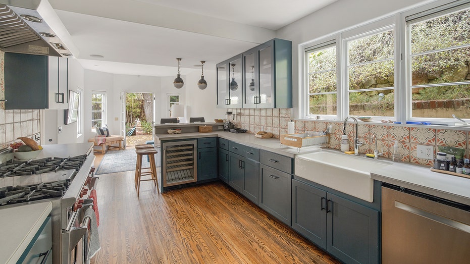 The kitchen features all blue cabinets, white countertops and a red-tiled backsplash.