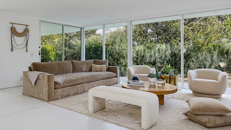 A family room with cream-colored furniture and floor to ceiling windows.