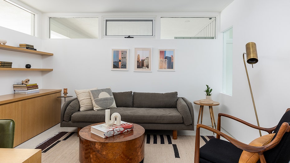 An office with built-in shelving a sofa and windows.