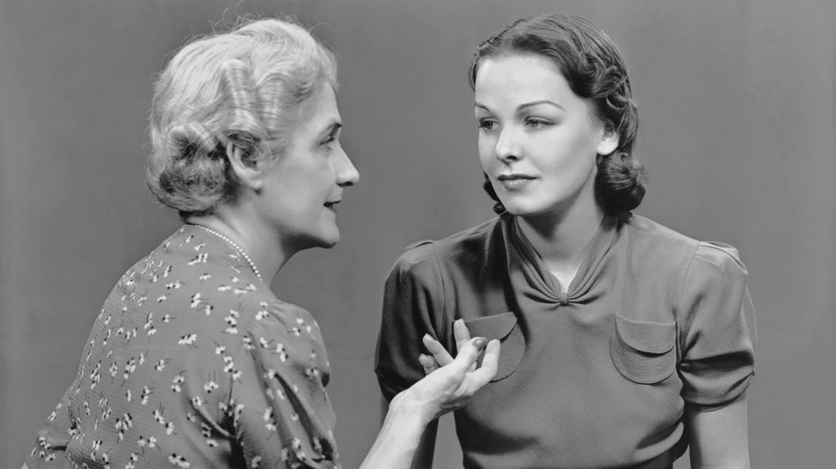 Black and white photo of parent talking to young adult in the 1950s