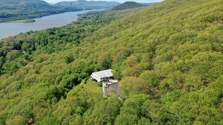 The home is surrounded by green trees and has perfect views of the Hudson River.