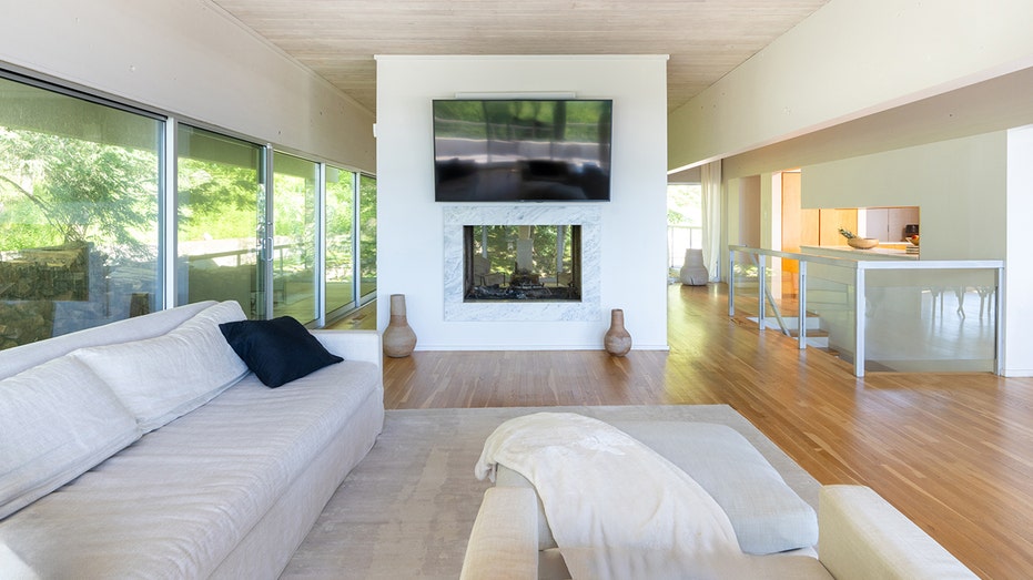 The home's living room features a double-sided fireplace, and is surrounded by floor to ceiling windows.