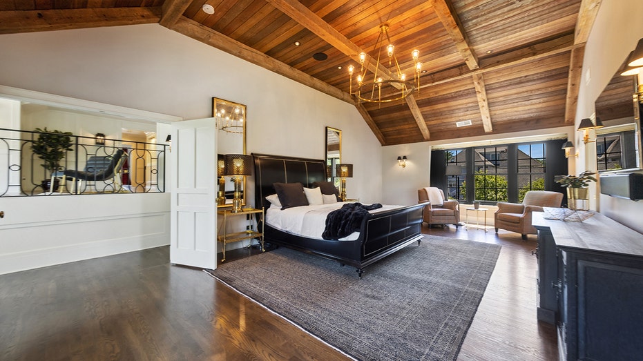 A spacious primary bedroom with wooden ceiling and big windows.