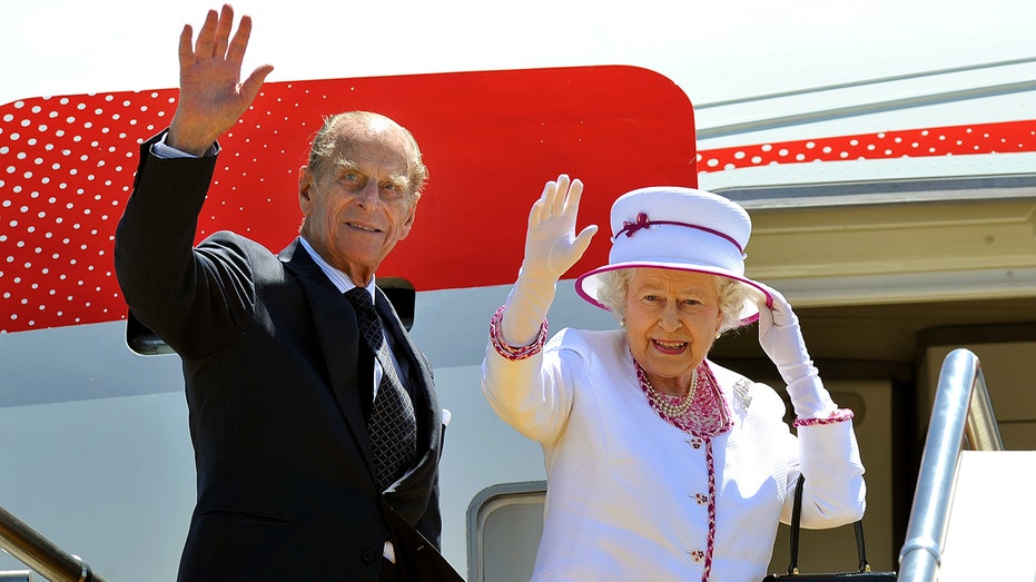 Queen Elizabeth and Prince Philip waving as they board a flight. 