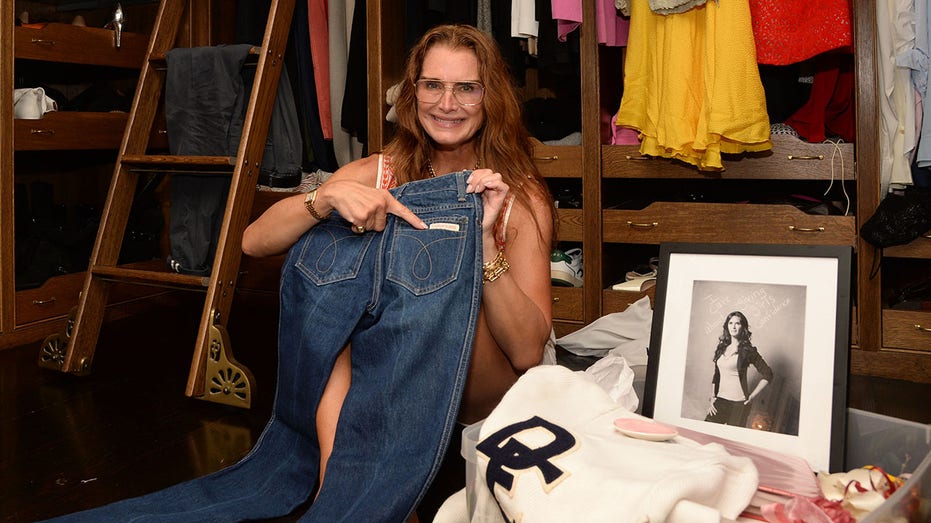 Brooke Shields smiles and points at the Calvin Klein logo on a pair of jeans