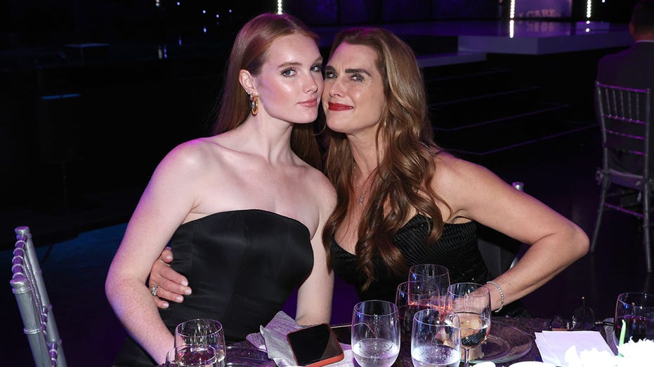 Grier Henchy in a black strapless dress soft smiles at a table with her mother, Brooke Shields, also in black