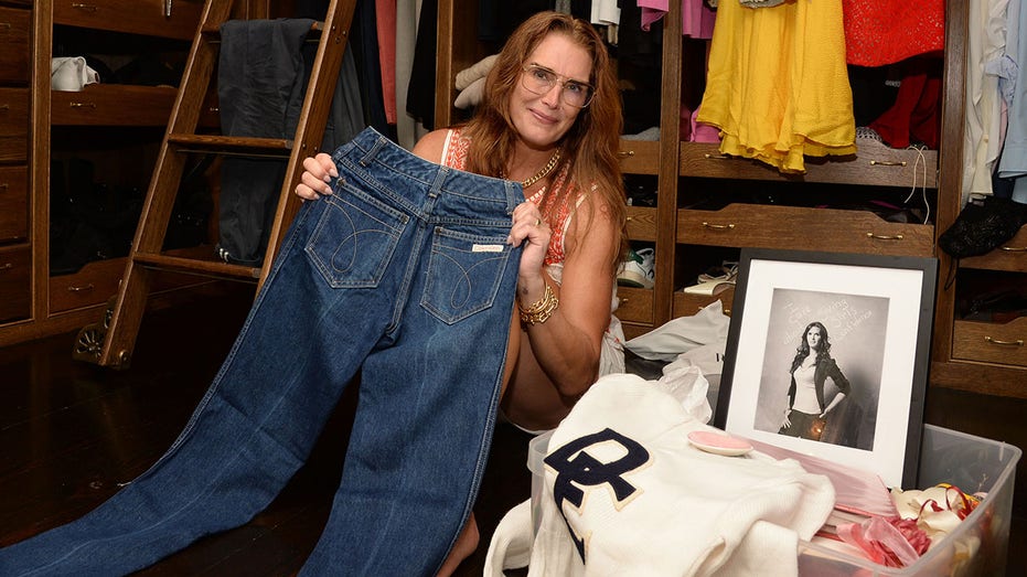 Brooke Shields soft smiles while holding up her blue Calvin Klein jeans