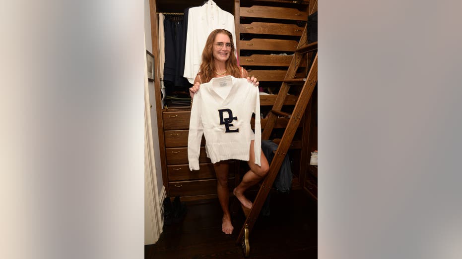 Brooke Shields smiles as she poses with her white sweater from high school