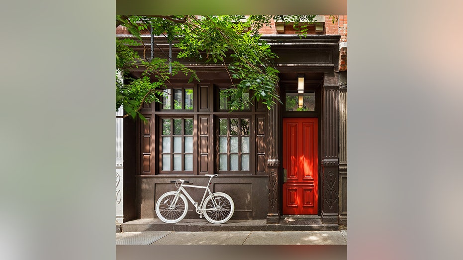 Exterior of the brown townhouse with a bright red door and bicycle outside