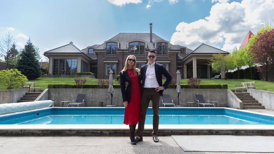 couple stands in front of pool and nice home