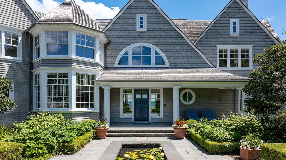 The exterior of the home is lined with trees and features a cobblestone courtyard and fountain.