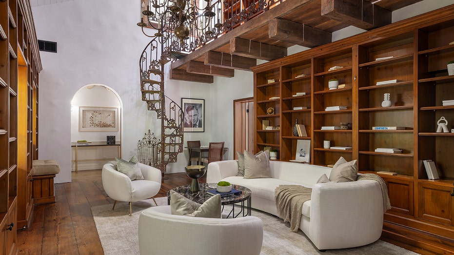 Spiral staircase leads into a room with a large bookshelf and more cream seating