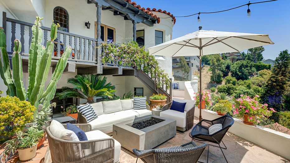 The backyard of the house includes a large sofa and fire pit, as well as a large umbrella to protect guests from the sun.