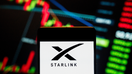 In this photo illustration, the American satellite internet constellation and subsidiary of the aerospace company SpaceX owned and operated by Elon Musk, Starlink, logo seen displayed on a smartphone with an economic stock exchange index graph in the background. 