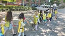 Children from Bright Horizons daycare hold onto a cord as they walk outside in New York City to ensure they stay together with their group and supervisor. Daycare is utilized by working parents, providing socialization, educational activities, playtime, and care designed to support children&apos;s development and prepare them for school.