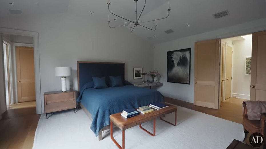 The bedroom features a bed with a blue comforter and a few lounge chairs.