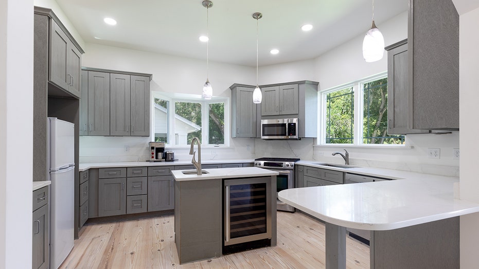 The modern kitchen in the guest house features gray cabinets and white countertops.