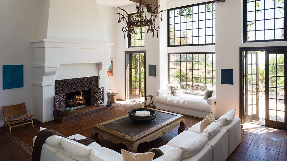 The living room boasts high ceilings with exposed wooden beams, a fireplace and multiple big windows.