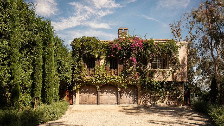 The exterior of the home is covered in vines and purple flowers.