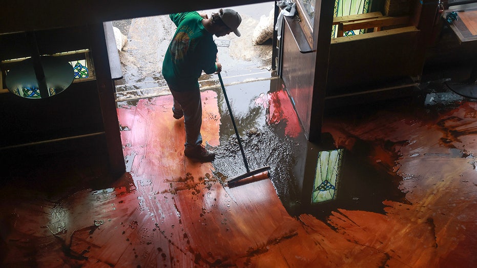 Austin Stolpe clears the mud from the floor of the Celtic Ray Public House restaurant/bar after it was inundated with flood waters when Hurricane Milton passed through the area