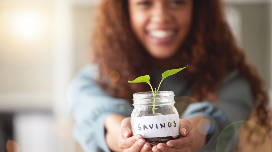 A woman holding a jar "savings" with a small plant growing high