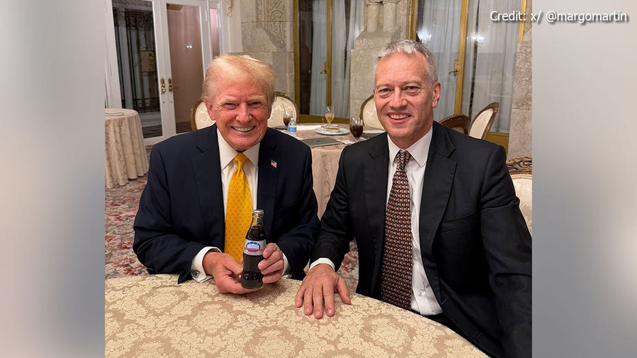 Donald Trump and James Quincey sit together as Trump holds up the first ever Presidential Commemorative Inaugural Diet Coke bottle.