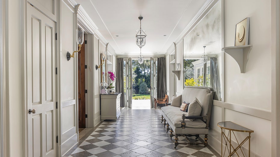 The entryway boasts black and white tiled floors, and a large mirror on the wall.