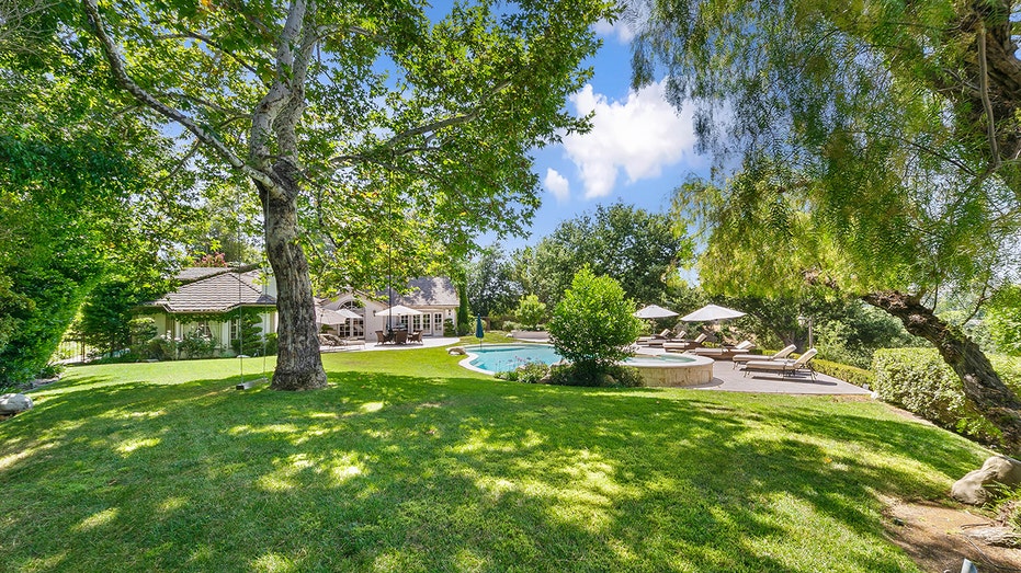 The home's backyard features large grass fields with trees and a swing.