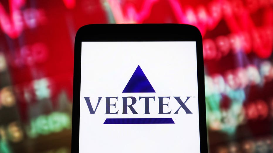 Ukraina - 2023/12/29: Dalam ilustrasi foto ini, logo Vertex Pharmaceuticals terlihat pada smartphone dan grafik pasar saham pada layar PC. (Ilustrasi foto oleh gambar pavlo gonchar/sopa/lightrocket melalui gambar getty)