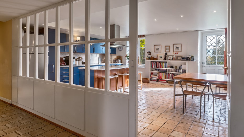 The kitchen is a central island, blue cabinets, a door to a casual dining area and beyond.