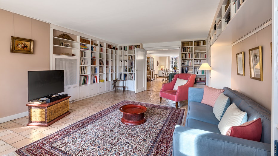 The library features a wall full of built-in bookshelves, pink and blue couches and a flat-screen TV.