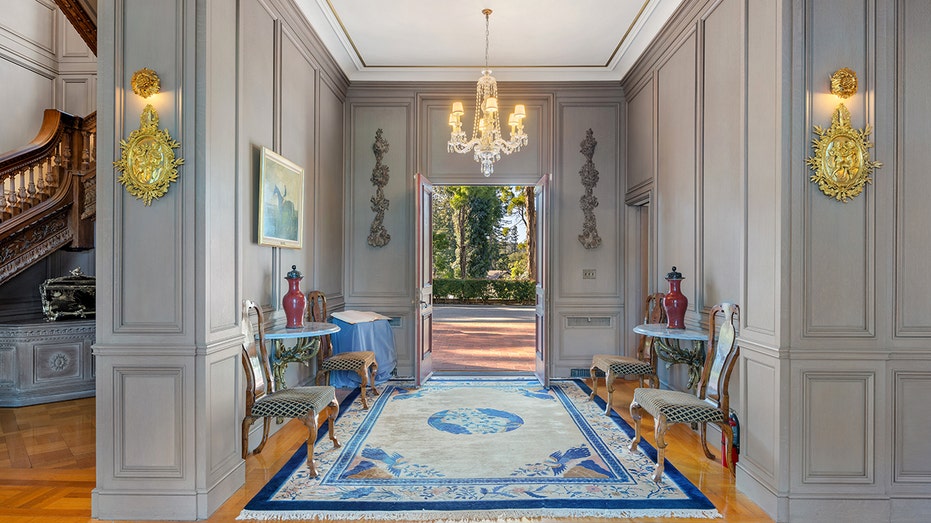 The front door opens onto a large fireplace with a chandelier and wooden floors.