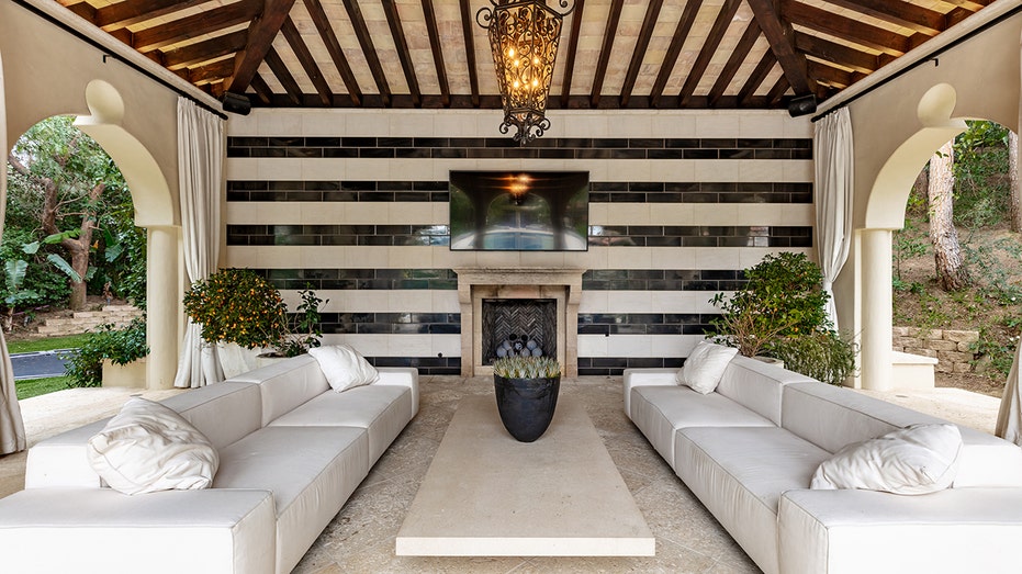 Just steps from the swimming pool is a cabana, which features a television and sofas.