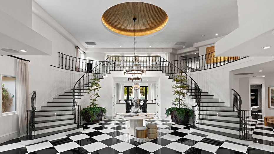 The foyer features a double staircase leading to the upper level and iconic black and white tile floors.