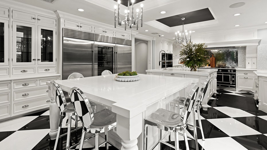 The entirely white kitchen includes two central islands and a transparent refrigerator.