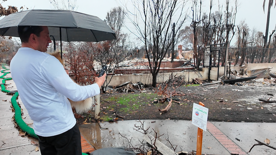 A man holds an umbrella, taking photos of a sign.