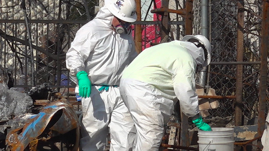 Two workers in costumes and danger gloves in the middle of a destroyed house